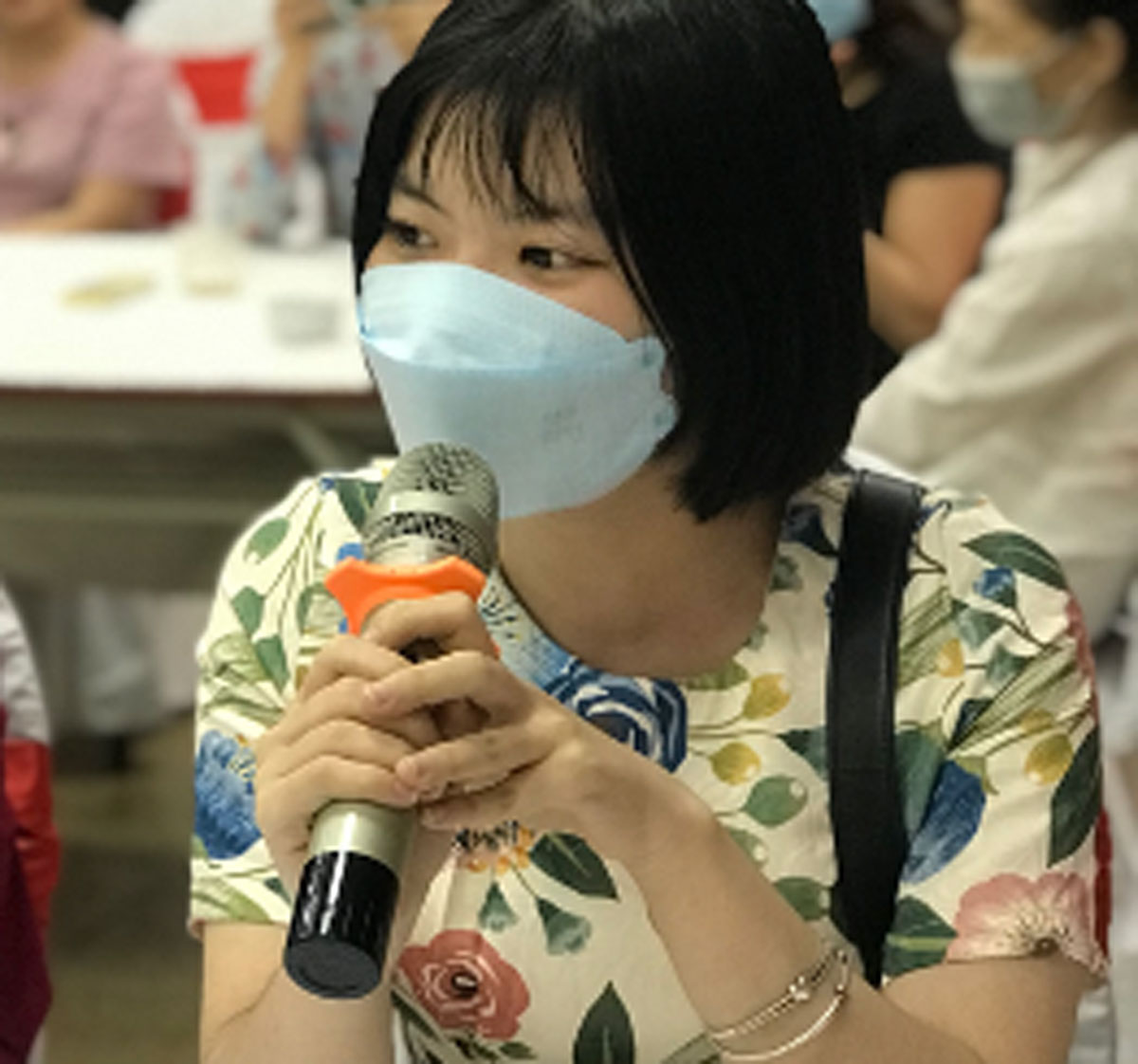 Texte alternatif : Une femme portant un masque parle dans un microphone.